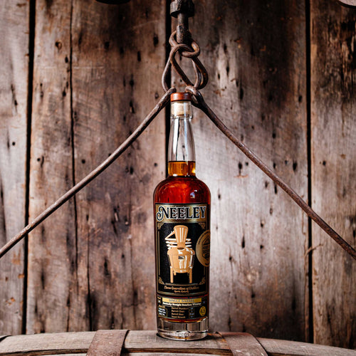 Bottle of Neeley Family Distillery Bottled-In-Bond Whiskey over a barrel