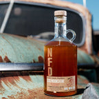 Bottle of Neeley Family Distillery Apple Pie Moonshine on a rusty vehicle with a blue sky background