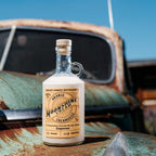 Bottle of Neeley Family Distillery Orange Creamsicle Moonshine on a rusty vehicle with a blue sky background