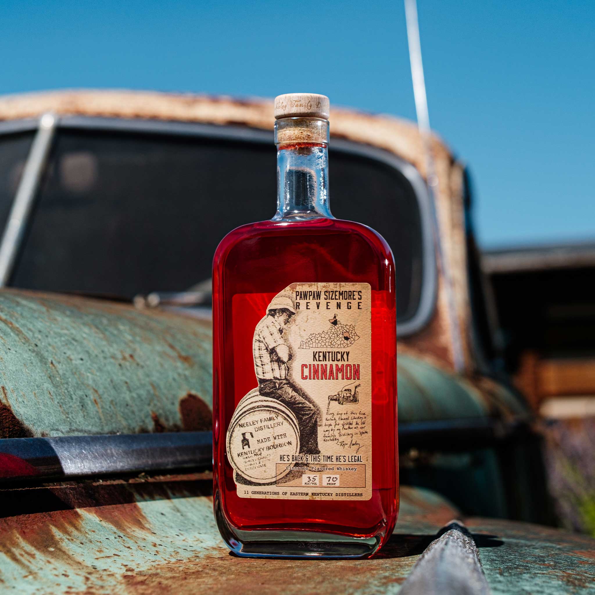 Bottle of Neeley Family Distillery Kentucky Cinnamon Flavored Whiskey on a rusty vehicle with a blue sky background