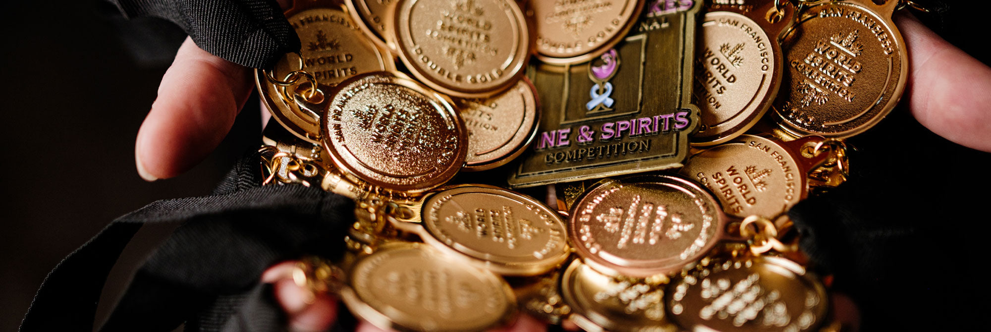 Collection of gold medals earned by Neeley Family Distillery held by hands against a dark background